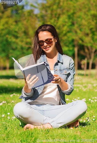 Image of smiling young girl with book sitting in park