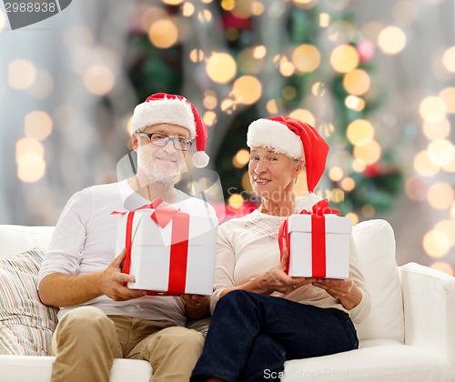 Image of happy senior couple in santa hats with gift boxes