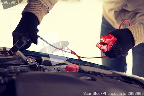 Image of closeup of man under bonnet with starter cables