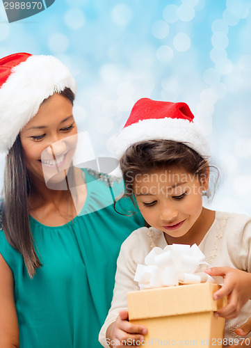 Image of happy mother and girl in santa hats with gift box