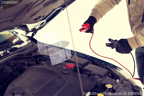 Image of closeup of man under bonnet with starter cables