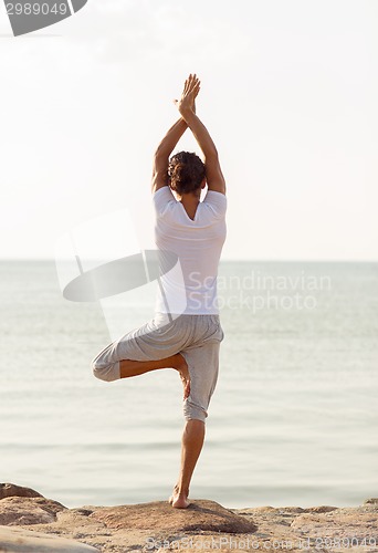 Image of young man making yoga exercises outdoors