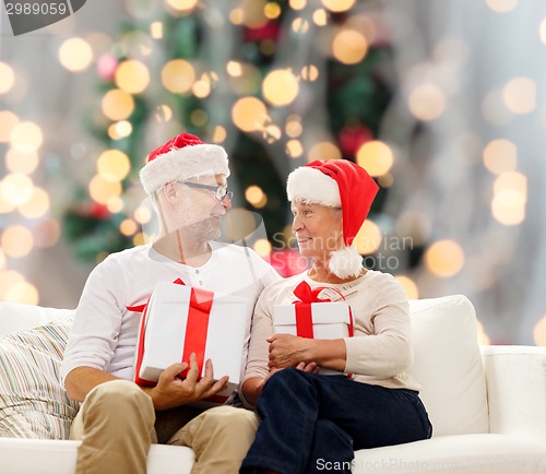 Image of happy senior couple in santa hats with gift boxes