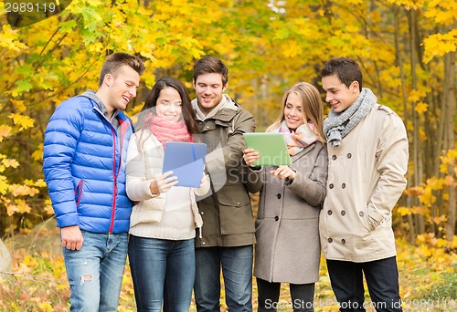 Image of group of smiling friends with tablets in park