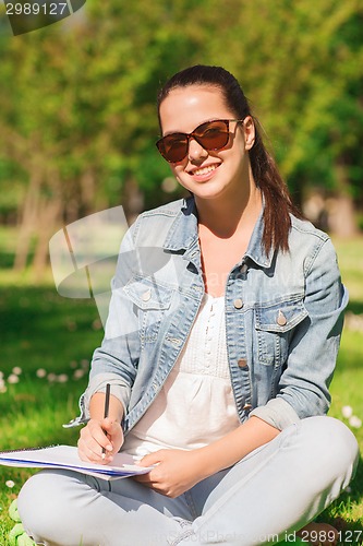 Image of smiling young girl with notebook writing in park