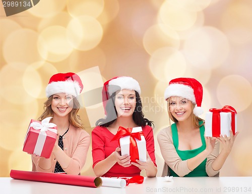 Image of smiling women in santa helper hats packing gifts