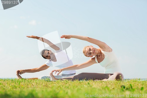 Image of smiling couple making yoga exercises outdoors