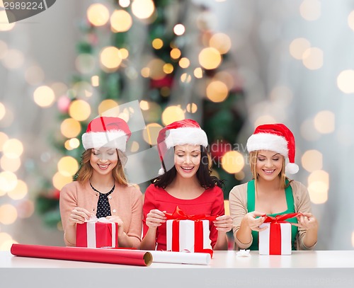 Image of smiling women in santa helper hats packing gifts