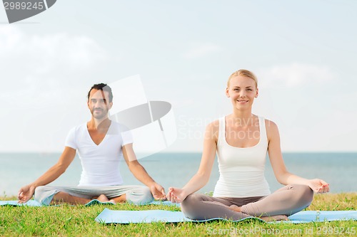 Image of smiling couple making yoga exercises outdoors