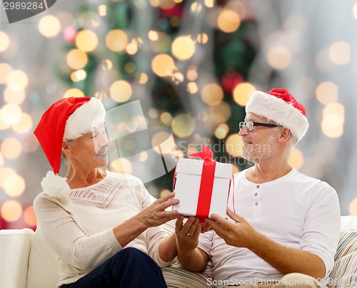 Image of happy senior couple in santa hats with gift box