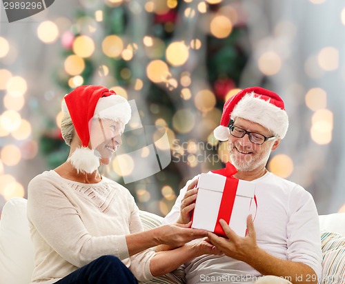 Image of happy senior couple in santa hats with gift box