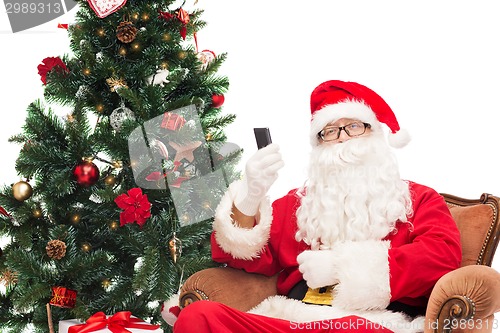 Image of santa claus with smartphone and christmas tree