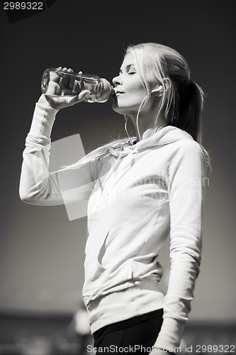Image of woman drinking water after doing sports outdoors