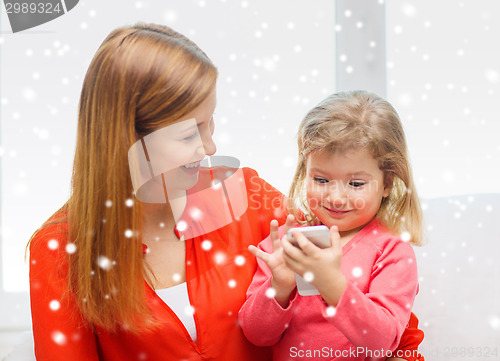 Image of happy mother and daughter with smartphone at home