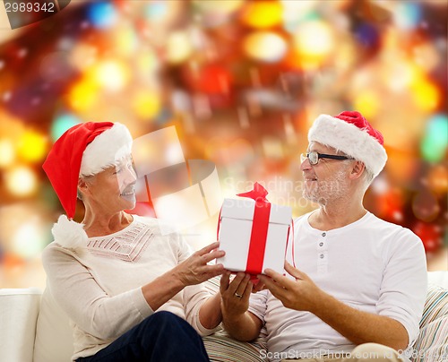 Image of happy senior couple in santa hats with gift box