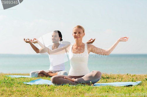 Image of smiling couple making yoga exercises outdoors