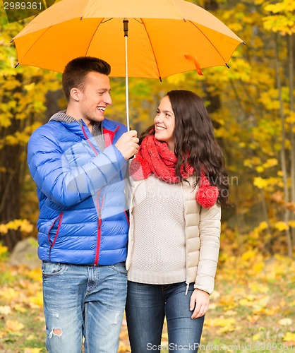 Image of smiling couple with umbrella in autumn park