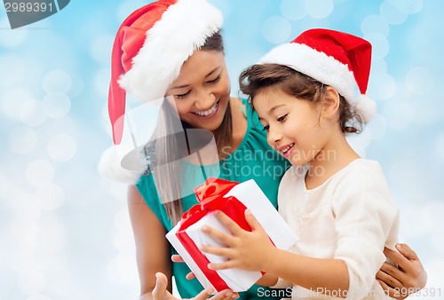 Image of happy mother and girl in santa hats with gift box