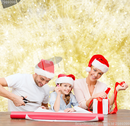 Image of happy family in santa helper hats packing gift