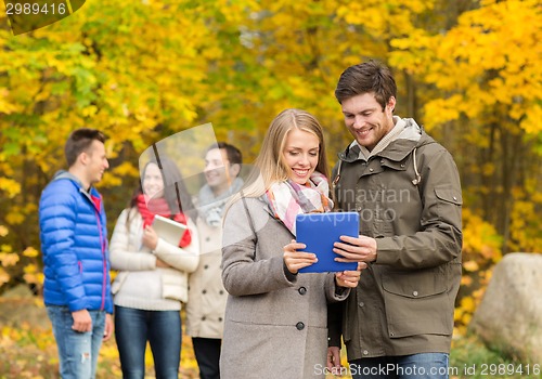 Image of group of smiling friends with tablets in park
