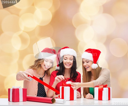 Image of smiling women in santa helper hats packing gifts