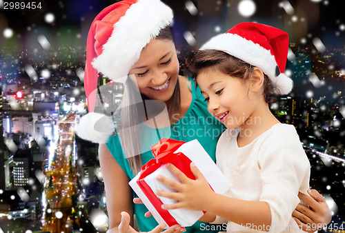 Image of happy mother and girl in santa hats with gift box