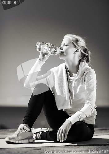 Image of woman drinking water after doing sports outdoors