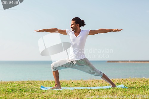 Image of smiling man making yoga exercises outdoors