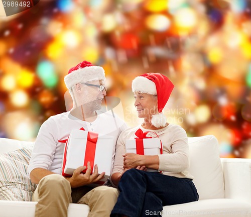 Image of happy senior couple in santa hats with gift boxes