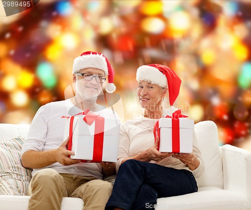 Image of happy senior couple in santa hats with gift boxes