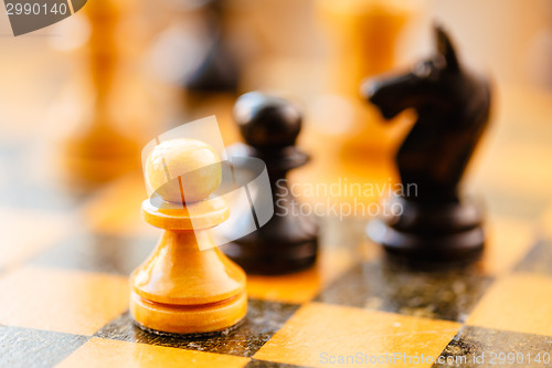 Image of White and black chess pawns and knight standing on chessboard