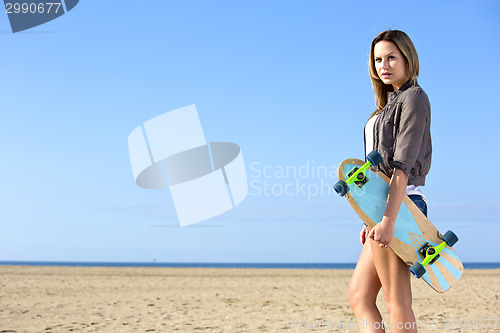 Image of Woman walking on a beach with a skateboard