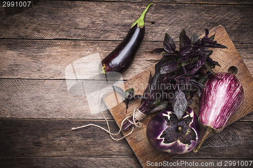 Image of Tasty Aubergines and basil on chopping board and wooden table