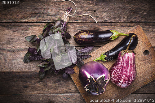 Image of Aubergines and basil on chopping board and wooden table