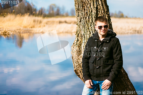 Image of Young Handsome Man Leaned Against Tree By River In Autumn Day. C