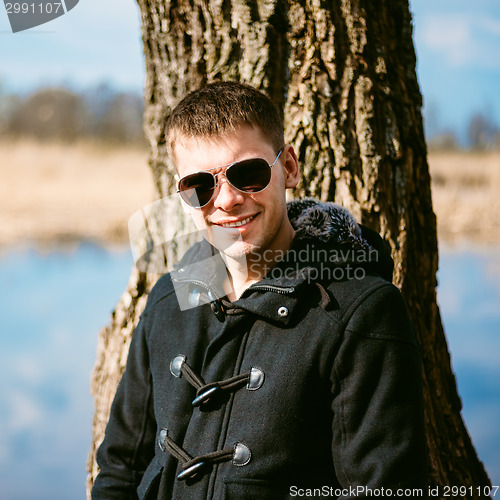 Image of Young Handsome Man Leaned Against Tree By River In Autumn Day. C