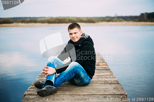 Image of Young Handsome Man Sitting On Wooden Pier, Relaxing, Thinking. C