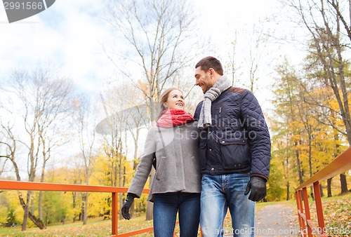 Image of smiling couple hugging on bridge in autumn park