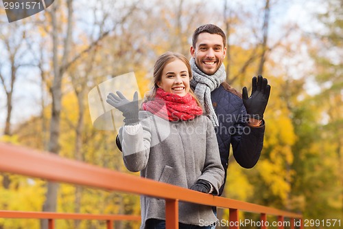 Image of smiling couple hugging on bridge in autumn park