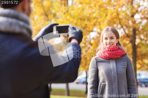 Image of smiling couple with smartphone in autumn park