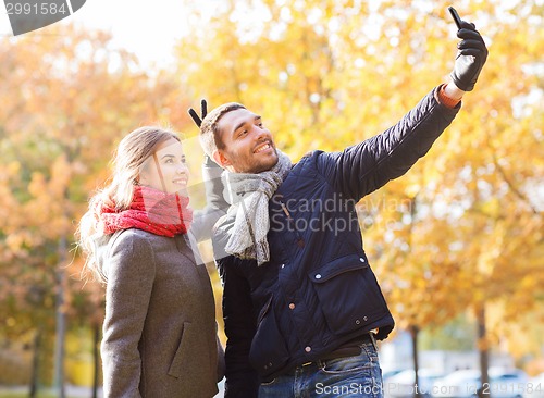 Image of smiling couple with smartphone in autumn park