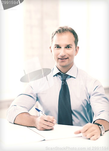 Image of handsome businessman writing in notebook