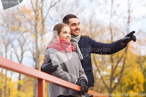 Image of smiling couple hugging on bridge in autumn park