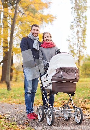 Image of smiling couple with baby pram in autumn park