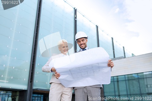 Image of smiling businessmen with blueprint and helmets