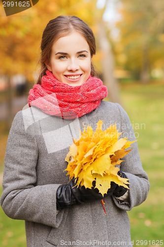 Image of smiling woman with bunch of leaves in autumn park