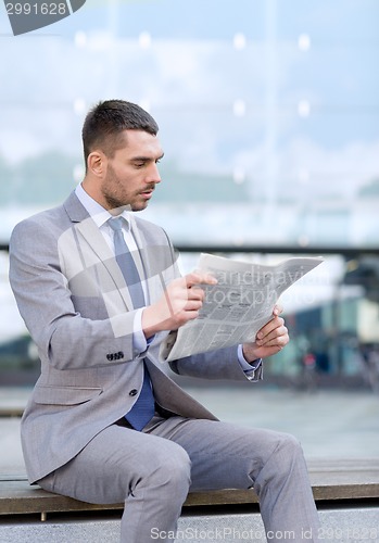 Image of young serious businessman newspaper outdoors