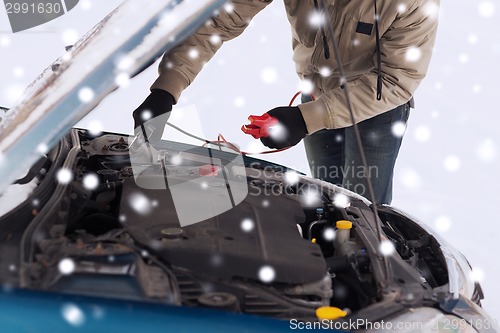 Image of closeup of man under bonnet with starter cables