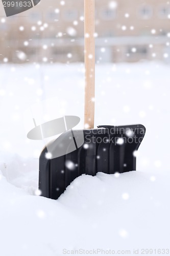 Image of black snowshowel with wooden handle in snow pile