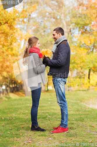 Image of smiling couple with bunch of leaves in autumn park